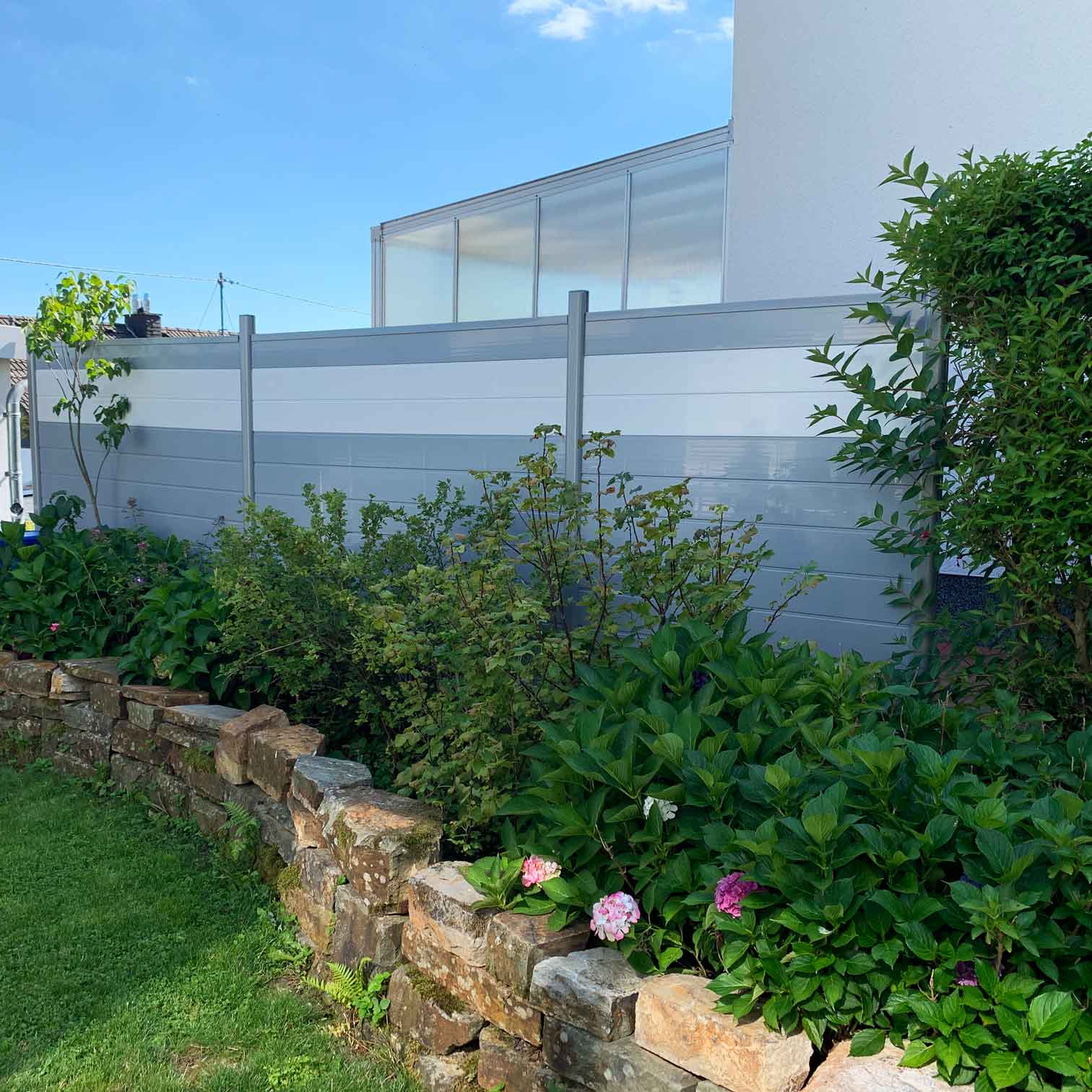 grauer Sichtschutzzaun mit weißem Streifen im Garten aus Kunststoff