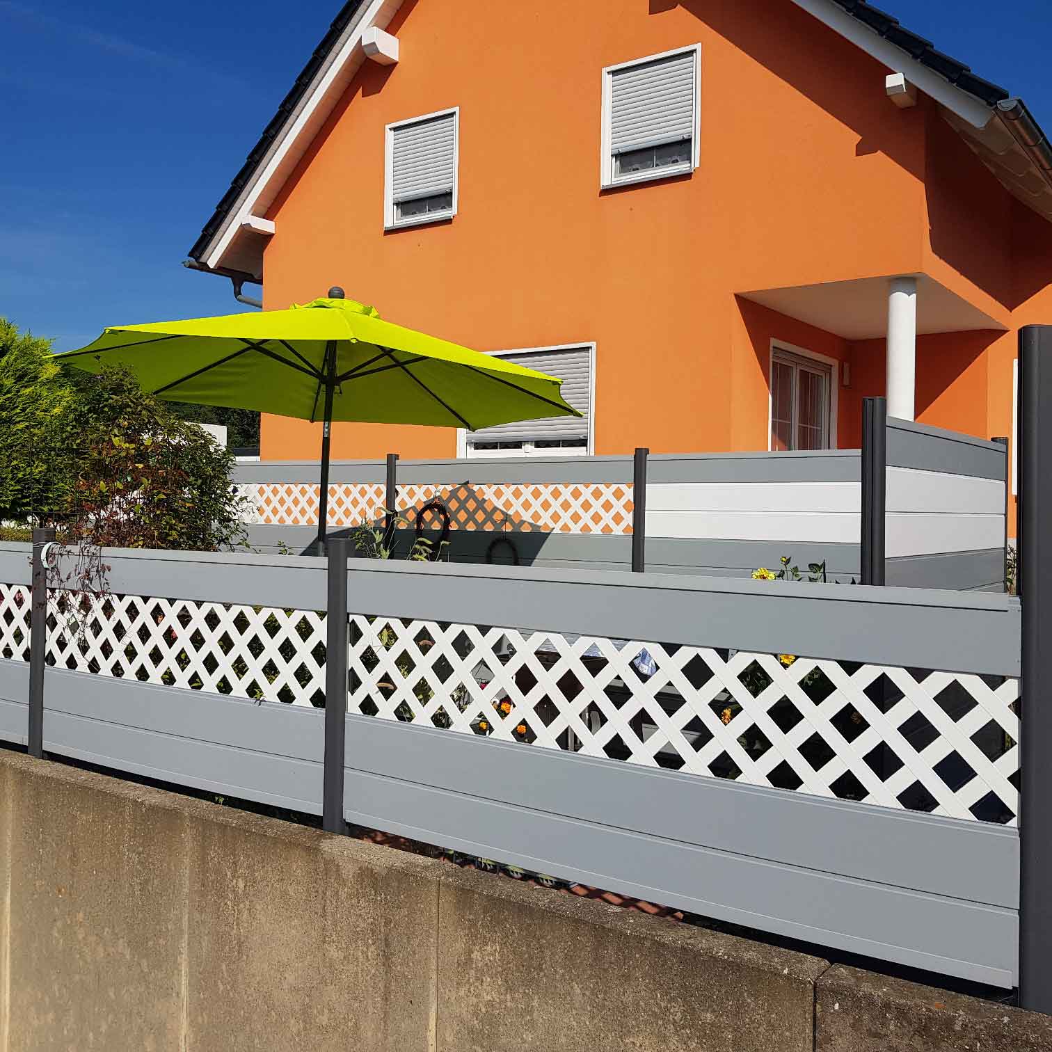 Mehrfarbiger Sichtschutz in Weiß, Grau und Anthrazit, mit Rankgitterelementen um eine Terrasse
